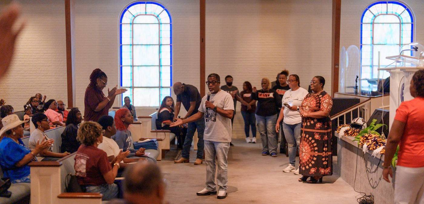 Members clapping in the pews beneath the arched windows of the Shiloh sanctuary